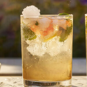 Two glasses of floral jasmine spritz bubbly cocktails blending jasmine tea, elderflower, grapefruit, and vodka, topped with prosecco and frozen edible flowers.