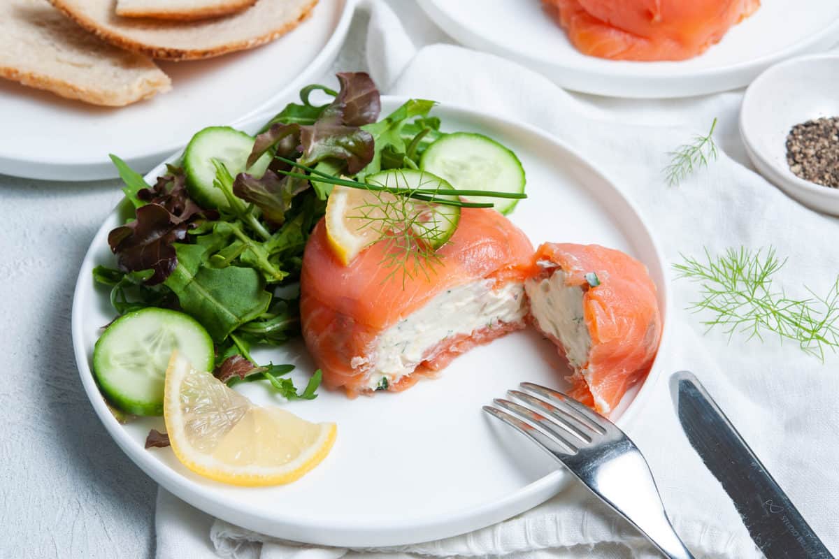 A smoked salmon appetizer shown on a plate next to a salad.
