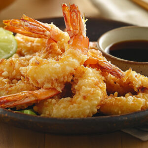 A photo showing tempura prawns on a plate with soy sauce and a wedge of lime.