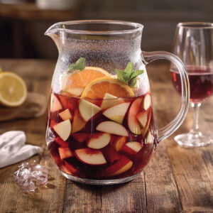 A photo showing a pitcher with sangria made from a sangria recipe. The pitcher is on a dark wooden table with 2 wine glasses filled with the drink.